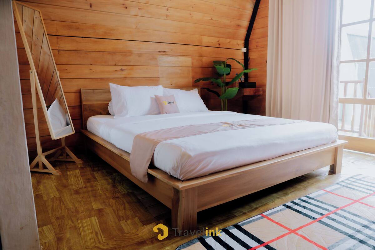 A wooden bedroom with a bed, a small table, and a plant.