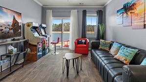 A modern living room with a leather sofa, a gaming console, a TV, and a view of the outdoors. - Central location Modern Lakefront 2 king-Suite 3 Bedroom 3 Full Bathroom (Myrtle Beach)