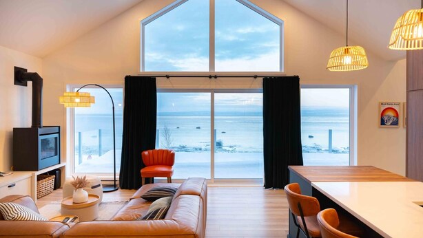 Uma sala de estar moderna com uma grande janela com vista para uma paisagem coberta de neve, um sofá aconchegante, uma área de jantar e uma lareira.