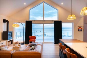 Un salon moderne doté d’une grande fenêtre donnant sur un paysage enneigé, d’un canapé confortable, d’un coin repas et d’une cheminée.