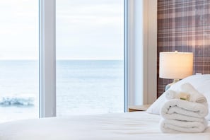 Hotellihuone, jossa on suuri ikkuna, josta avautuu näkymä merelle, siististi pedattu sänky valkoisilla lakanoilla ja yöpöydällä oleva lamppu.