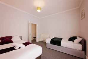 A hotel room with two beds, a radiator, and a door leading to another room.