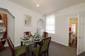 A dining area with a table set for four, chairs, a mirror, and a window with curtains.