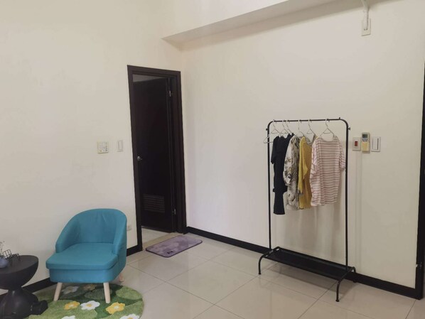 A room with a blue chair, a clothing rack with various garments, a black door, and a small table with a plant.