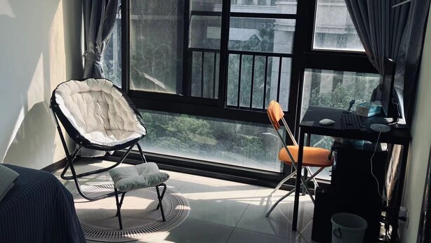 Una habitación moderna con ventanas amplias, un escritorio, una silla acolchada y una alfombra pequeña.