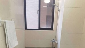 Un baño con bañera, ventana, toalla, una bolsa verde y una alfombra.