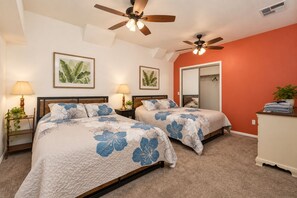 A bedroom with two beds, ceiling fans, bedside lamps, a mirror, and a dresser.