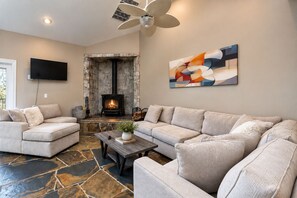 A living room with a stone fireplace, a large sofa, a coffee table, and a painting on the wall. - Yosemite & Bass Lake 6 bedrooms, sleeps 18 - Coarsegold Villa (Coarsegold)