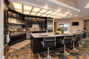 A modern kitchen with dark cabinetry, a central island with bar stools, and a stone tile floor.