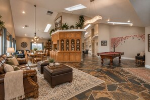 A spacious living room with a pool table, leather furniture, and a large wooden cabinet.