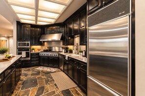 Une cuisine moderne avec des meubles de couleur sombre, des appareils en acier inoxydable et un sol en pierre à motifs.