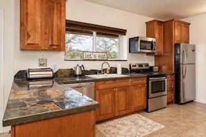 A modern kitchen with wooden cabinets, a stone countertop, stainless steel appliances, and a window with a view.