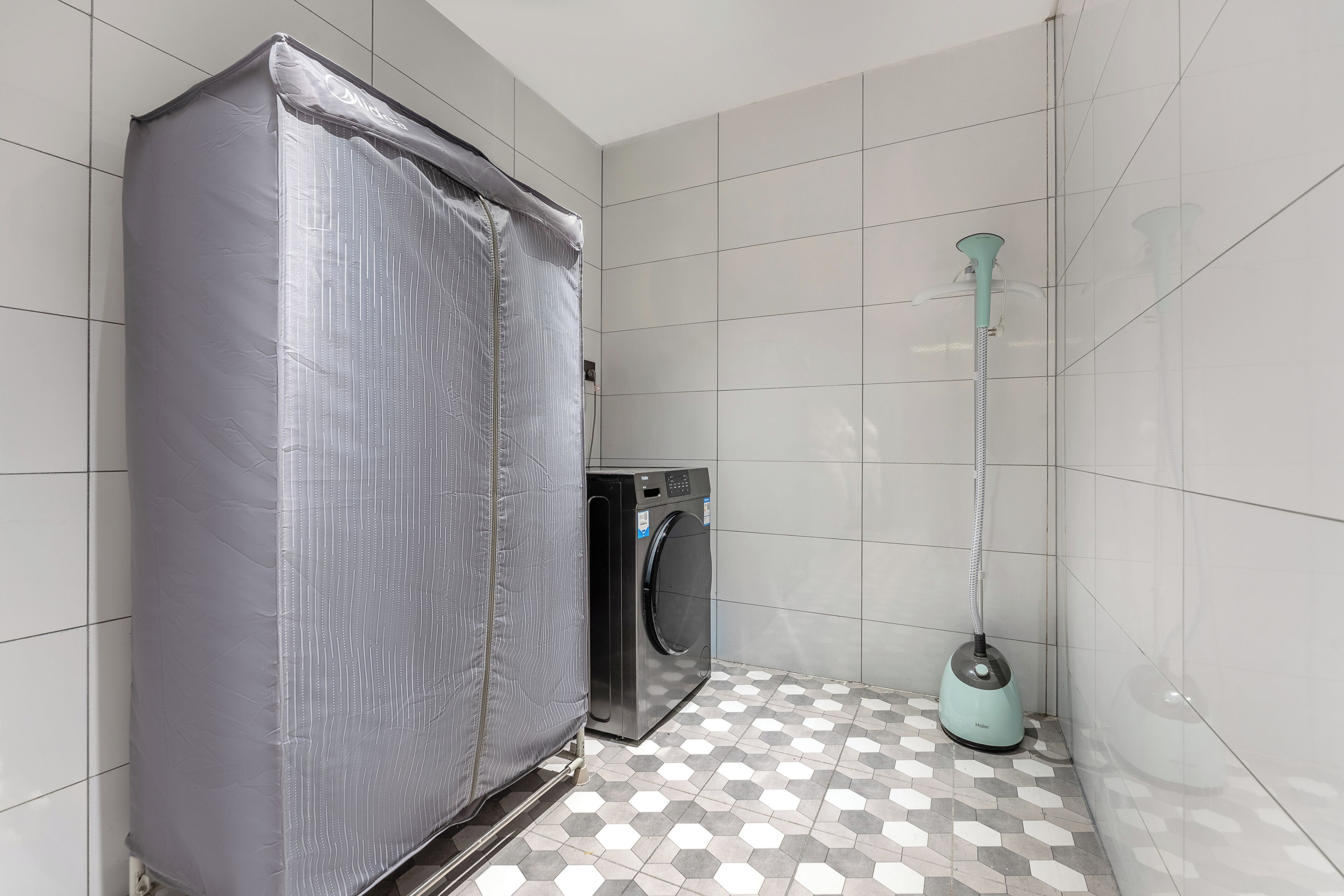 Un baño con piso de baldosas, lavadora y electrodoméstico cubierto.