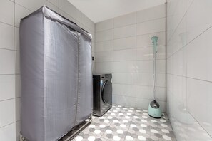 Un baño con piso de baldosas, lavadora y electrodoméstico cubierto.