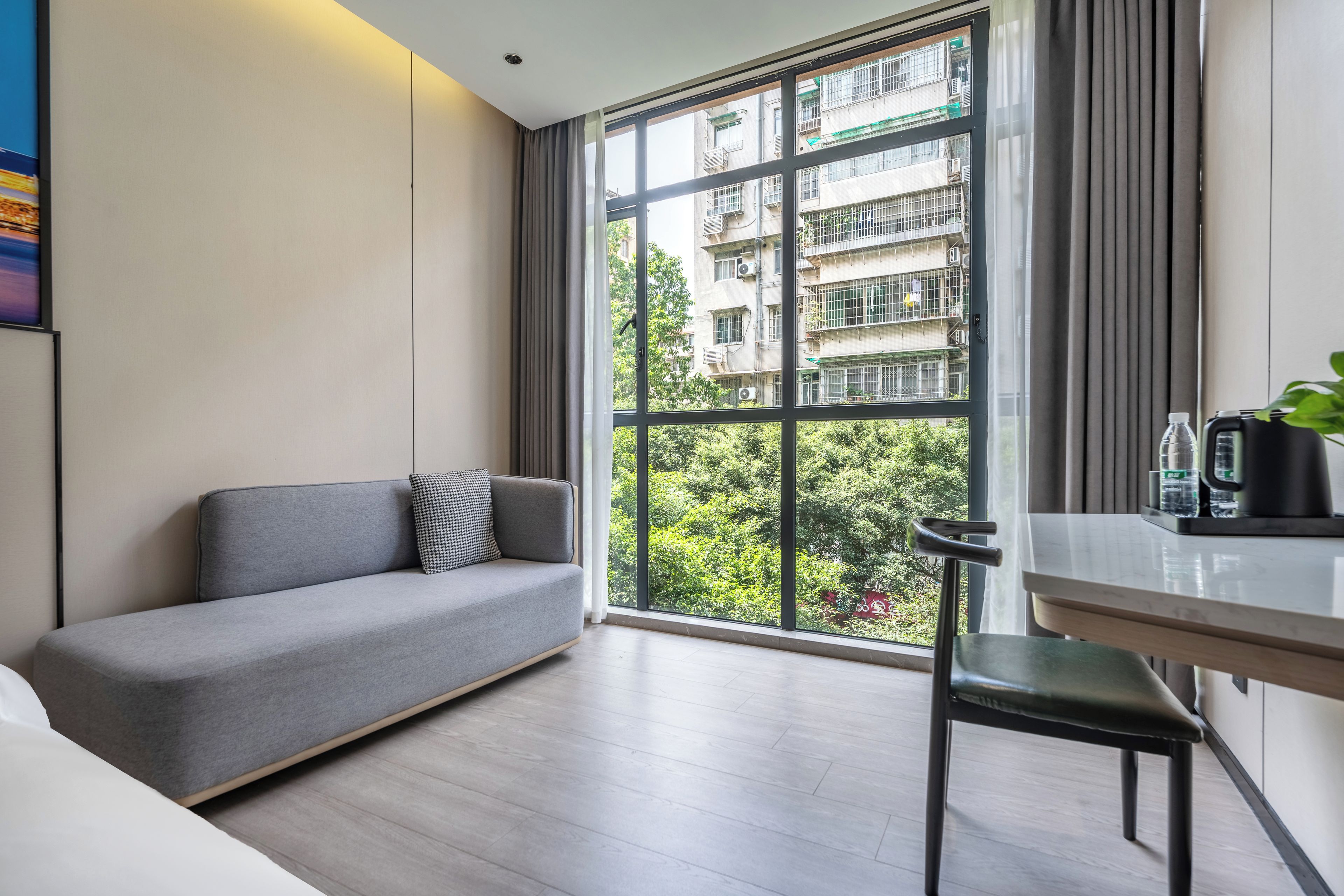A modern living room with a grey sofa, a dining table with chairs, and a large window offering a view of a residential building.