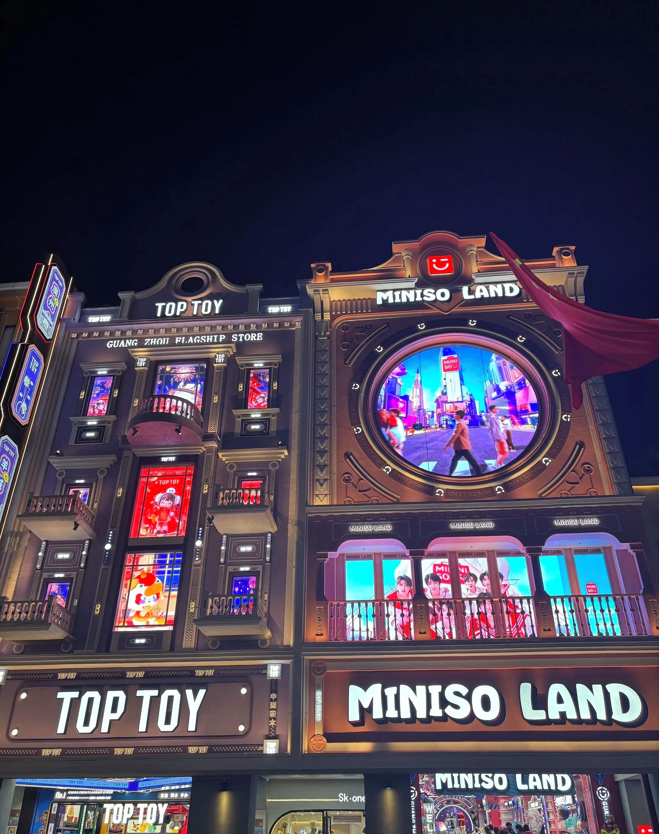 A building facade with illuminated signs for 'TOP TOY' and 'MINISO LAND'.