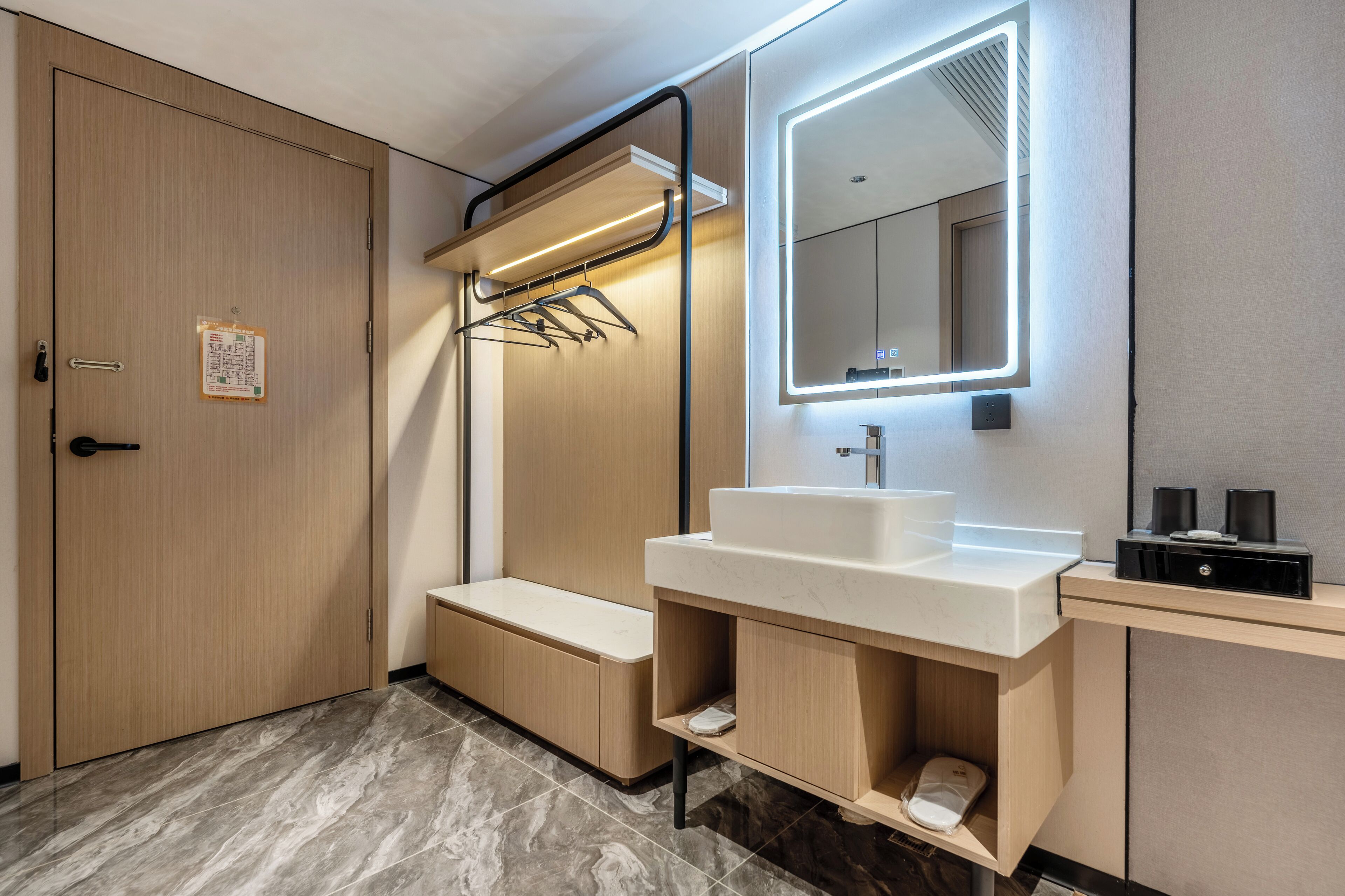 Une salle de bain moderne avec un meuble-lavabo en bois, un grand miroir doté d’un éclairage intégré et un porte-serviettes.