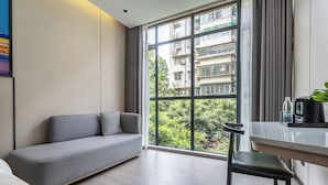 A modern living room with a grey sofa, a dining table with chairs, and a large window offering a view of a residential building. - Norman Hotel - Binjiang East Road Subway Station, Haizhu District, Guangzhou - Free shuttle service during the Canton Fair (Guangzhou)