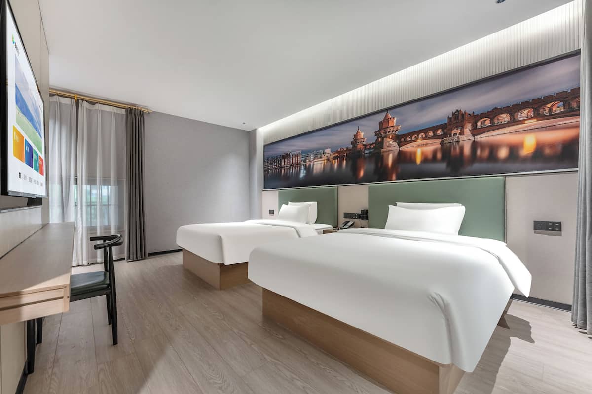 Una habitación de hotel con dos camas, un escritorio y un cuadro grande con una vista urbana.