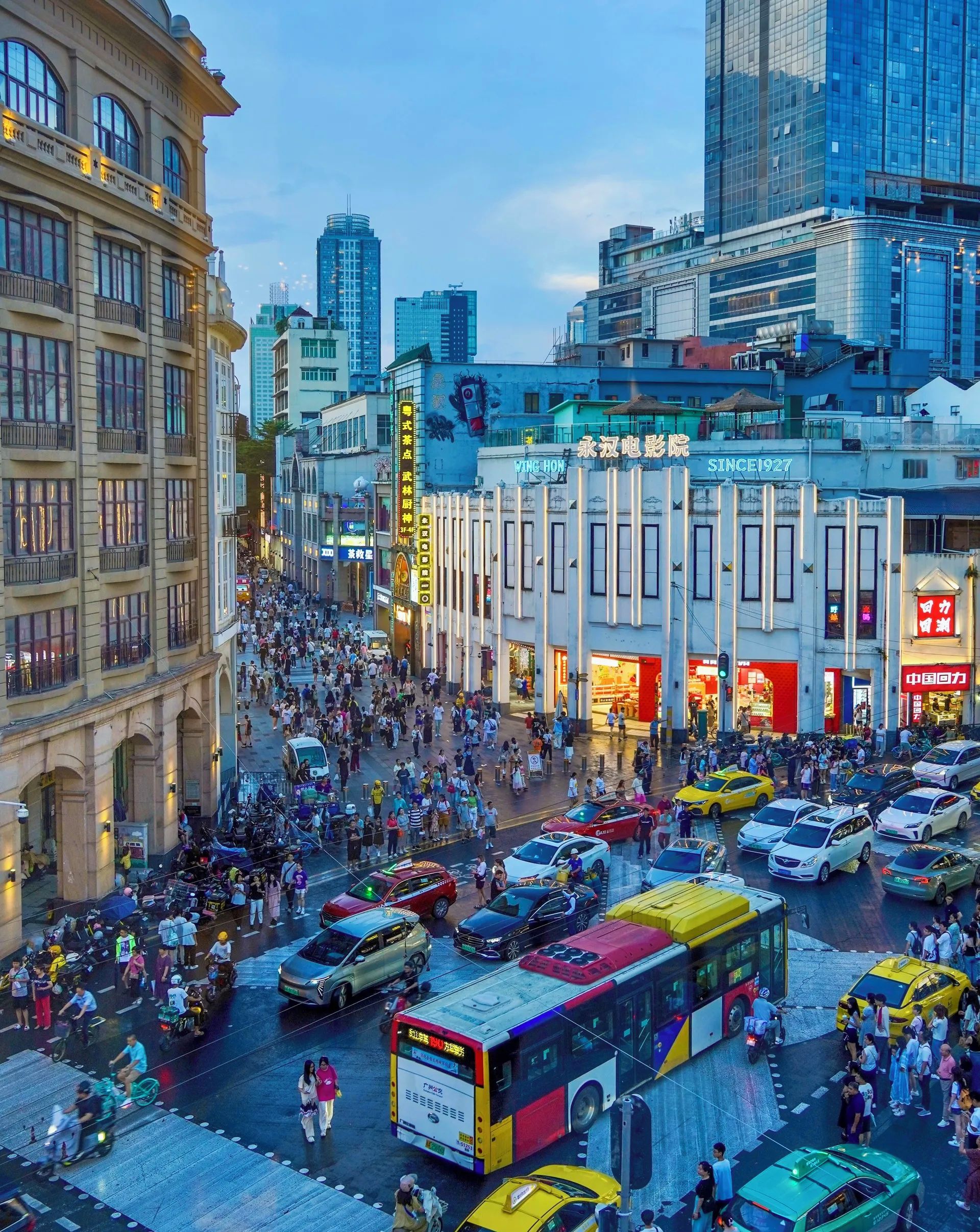 Una calle urbana concurrida, con peatones, vehículos y edificios comerciales.