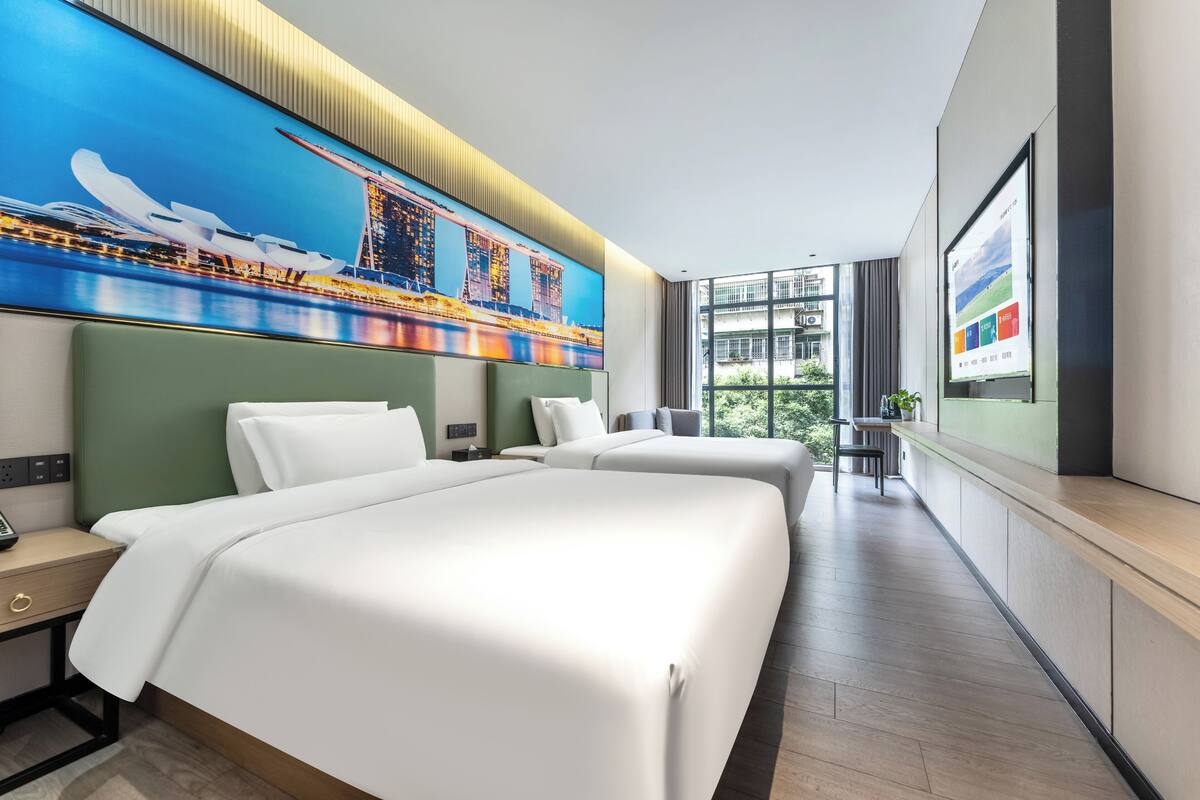 Habitación de hotel moderna con dos camas grandes, un ventanal con vistas a zonas verdes y un televisor de pantalla plana en la pared.