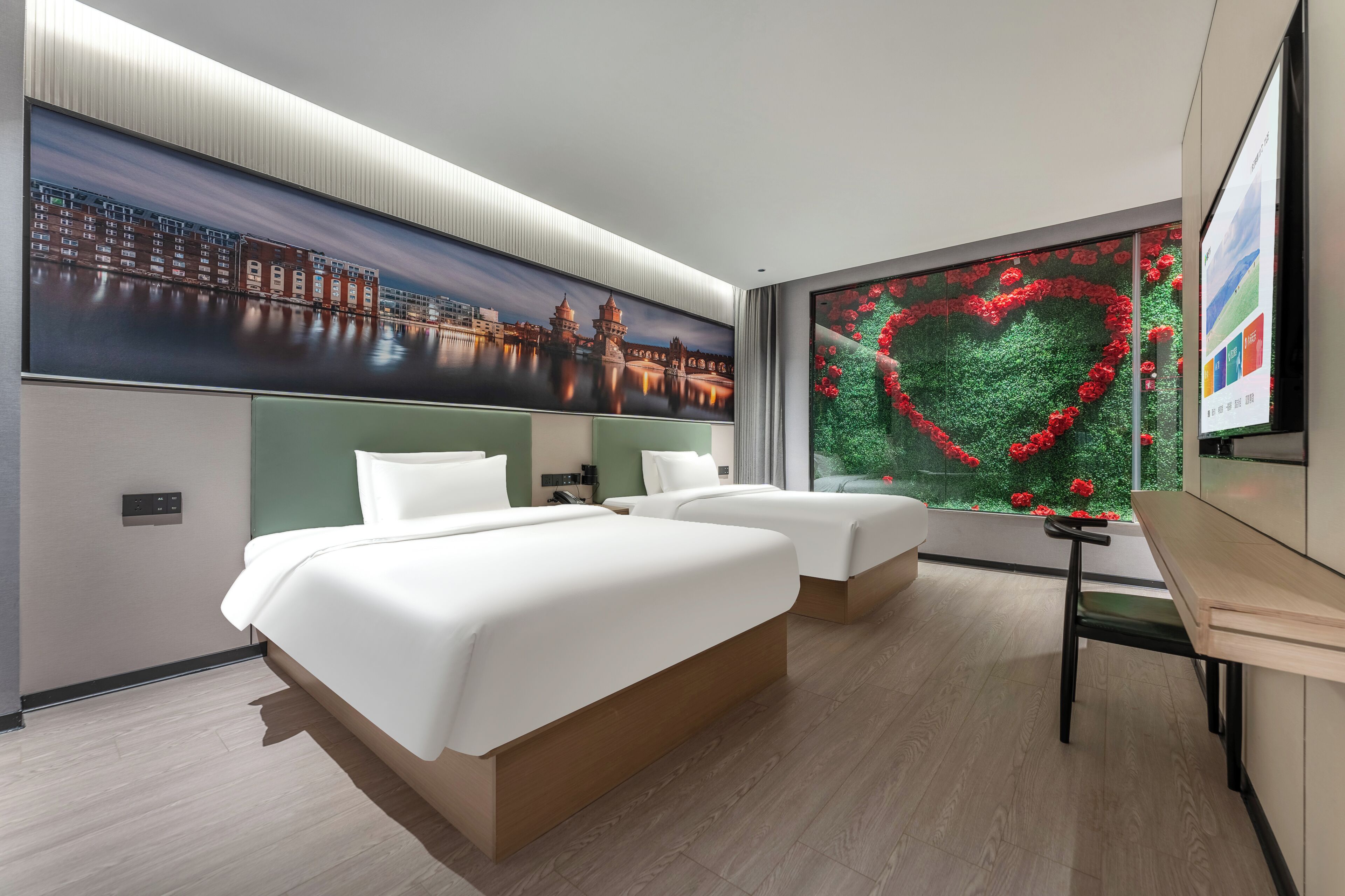 Una habitación de hotel con dos camas, un ventanal con decoración floral en forma de corazón y un mural con un paisaje urbano en la pared.