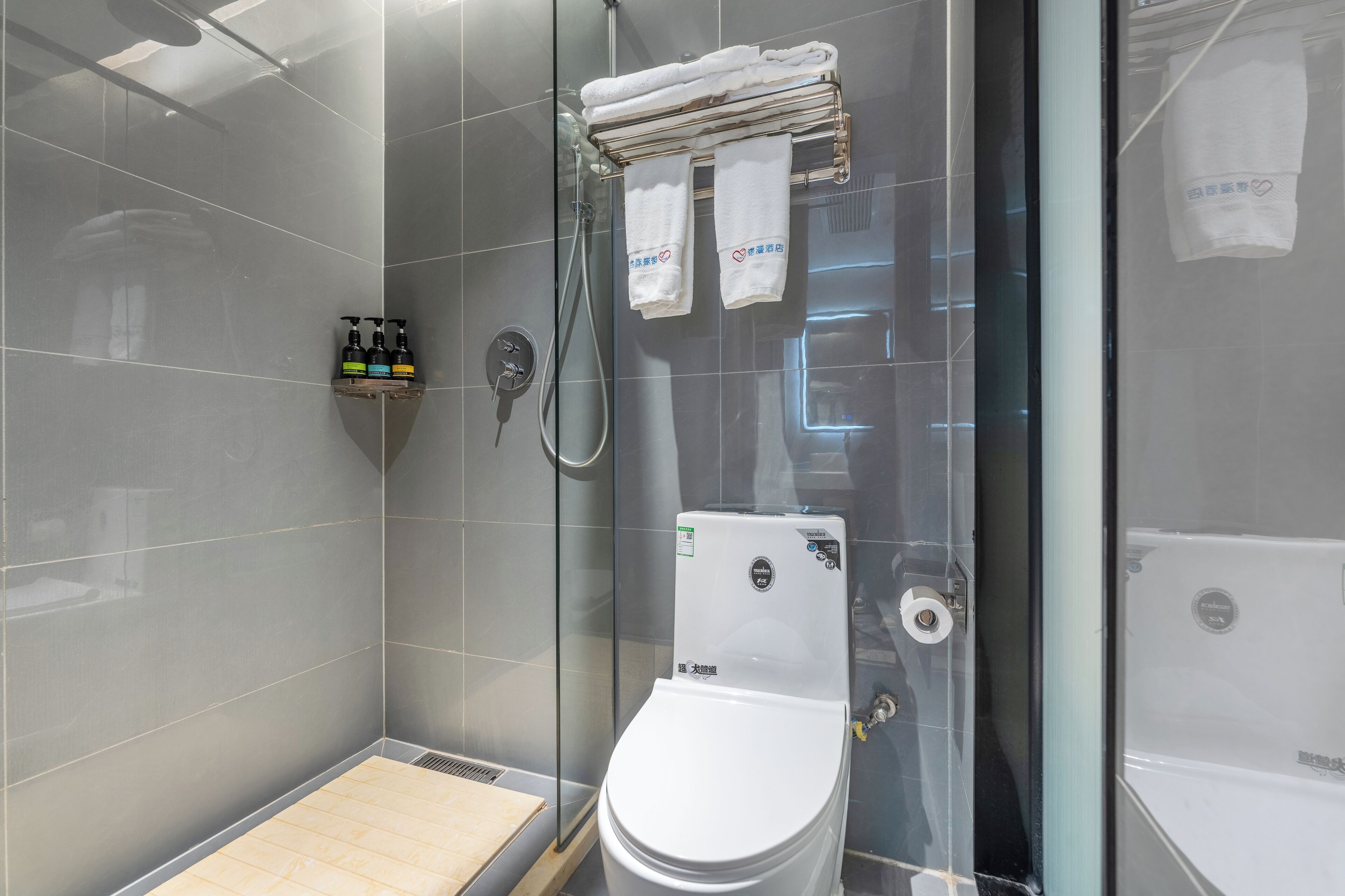 A modern bathroom with a glass-enclosed shower, a white toilet, and a towel rack with folded towels.