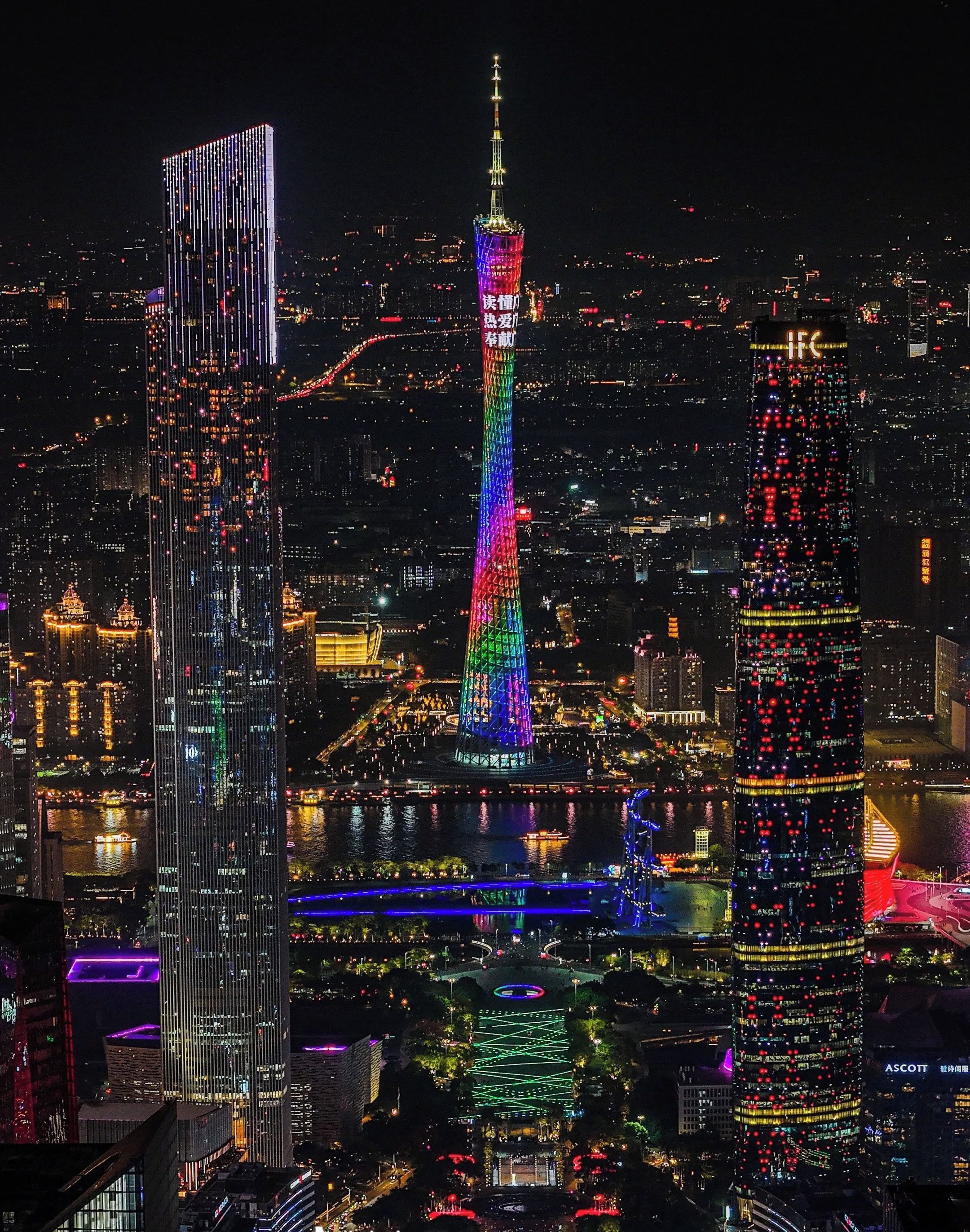 A nighttime cityscape with illuminated skyscrapers and a river.