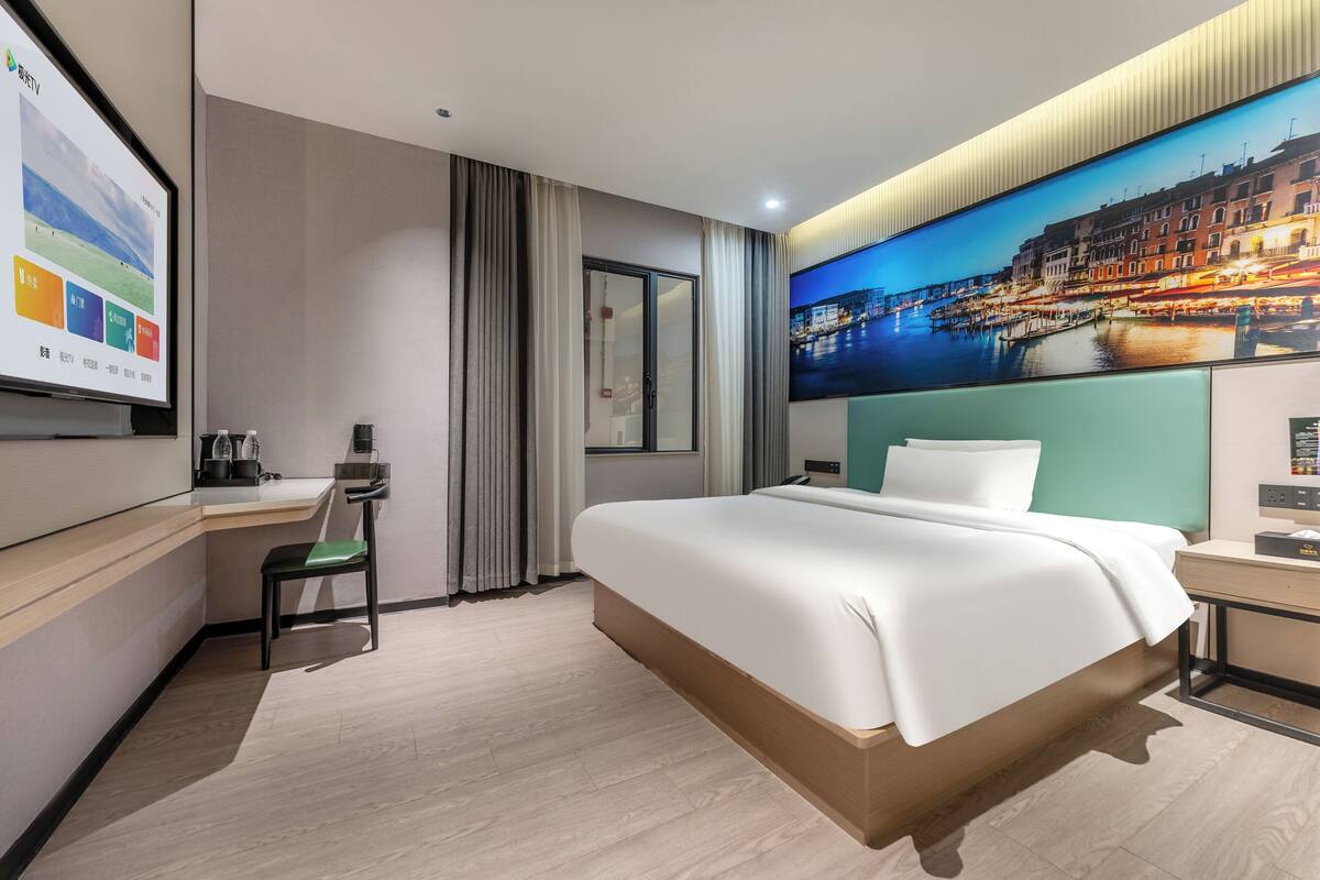 Una habitación de hotel moderna con una cama grande, un escritorio y una pantalla de televisión mostrando una presentación.