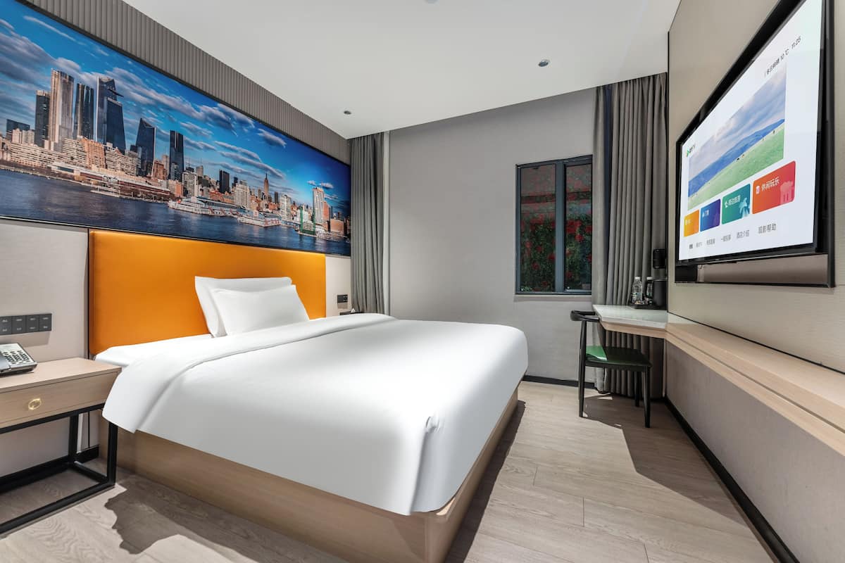 Una habitación de hotel moderna con una cama grande, un escritorio y un cuadro de un paisaje urbano en la pared.