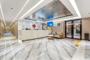 Un área de recepción moderna en un hotel, con suelo de mármol, mostrador de recepción, zona de estar y un techo con un diseño texturizado único.
