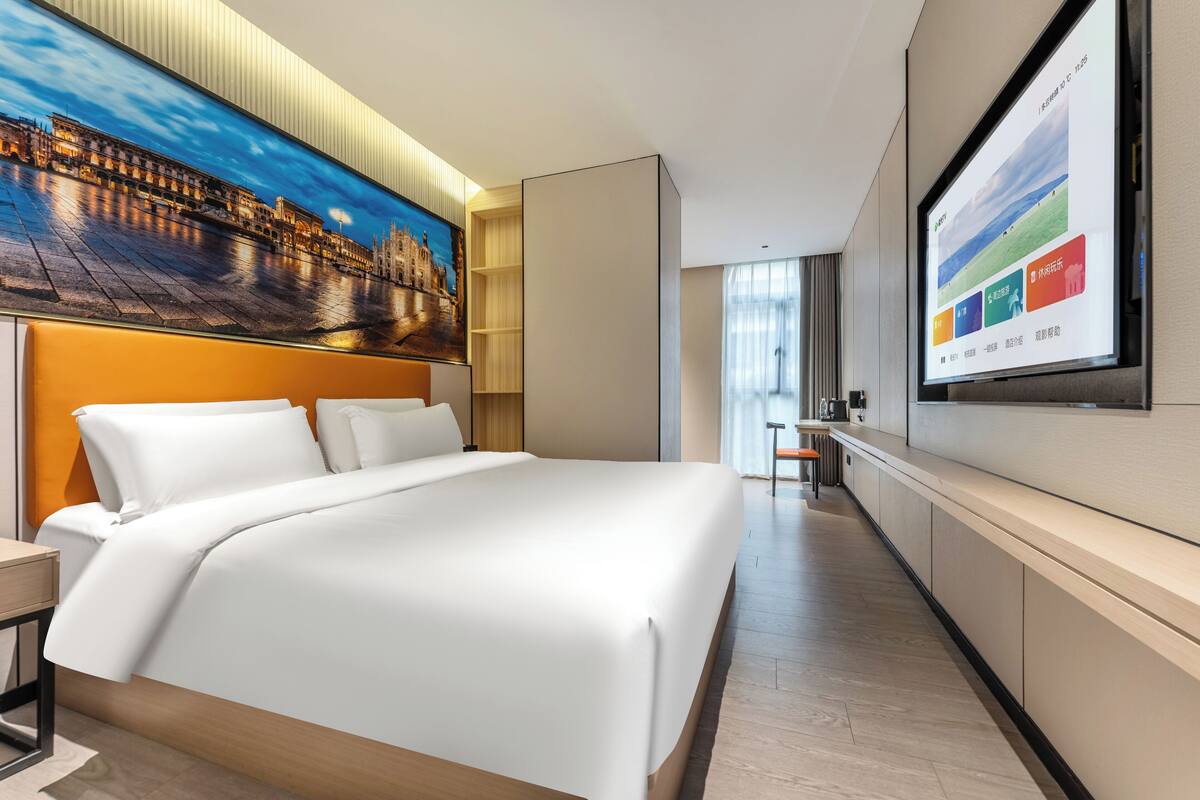 Una habitación de hotel moderna con una cama grande, un televisor de pantalla plana montado en la pared y un cuadro con una vista urbana sobre la cama.