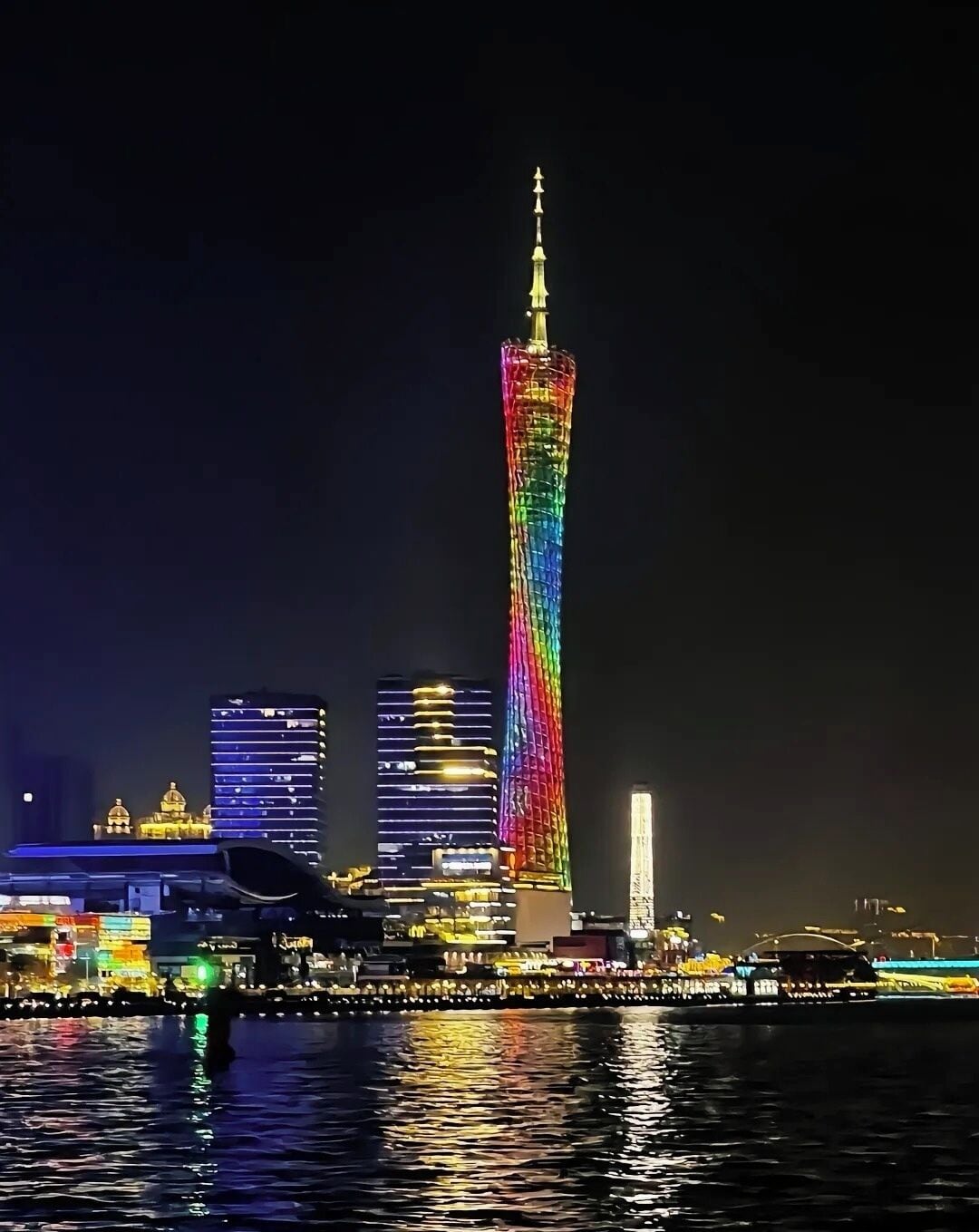 A city skyline at night with a prominent tower illuminated in rainbow colors.