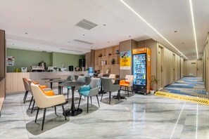 A hotel lobby with a reception desk, seating area, vending machine, and a blue carpeted corridor. - Norman Hotel - Free shuttle bus service during the Canton Fair-Free buffet breakfast-Free self-service laundry and drying (Guangzhou)