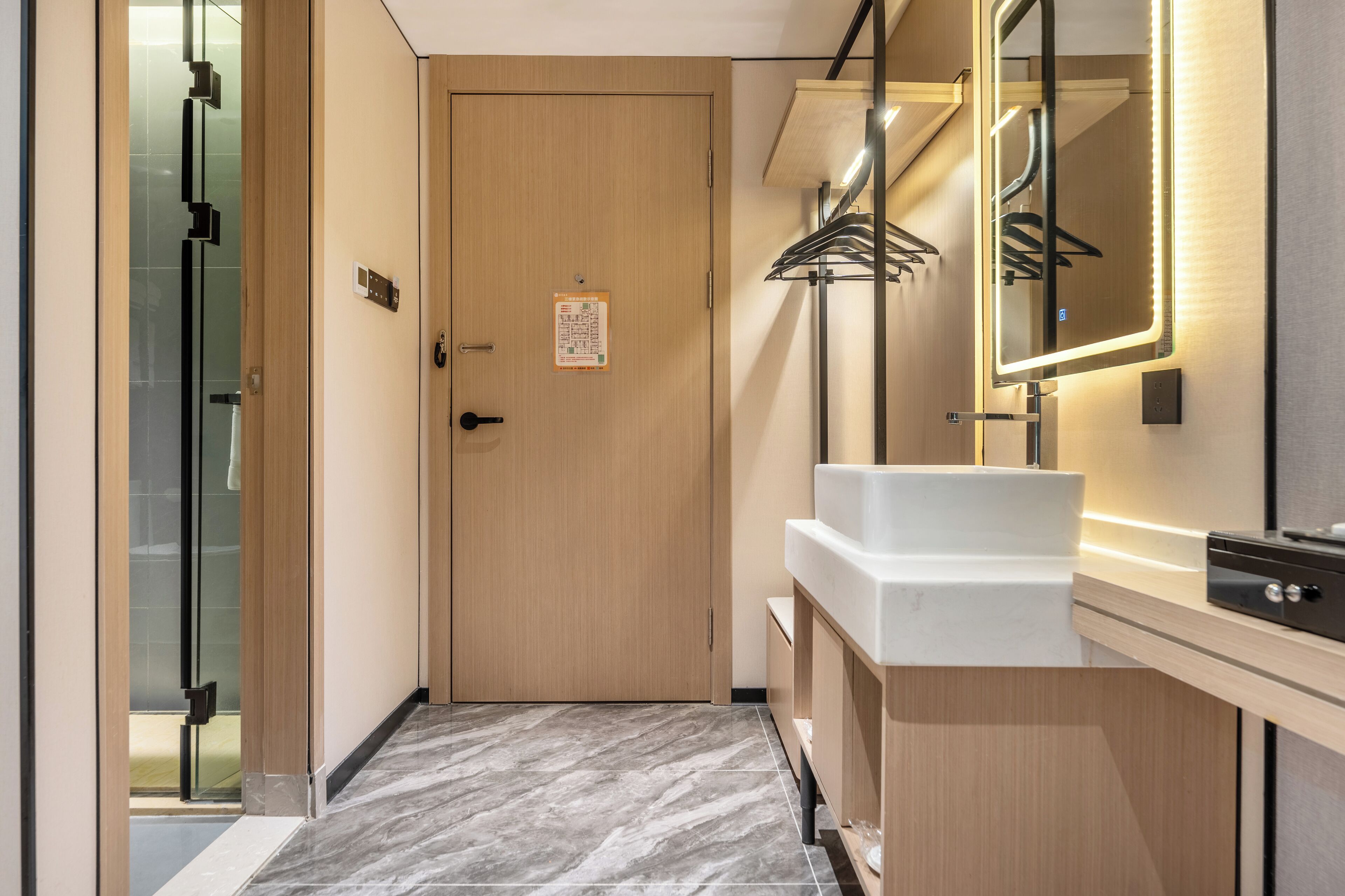 A modern bathroom with a wooden door, a white sink, a mirror with LED lights, and a glass shower enclosure.