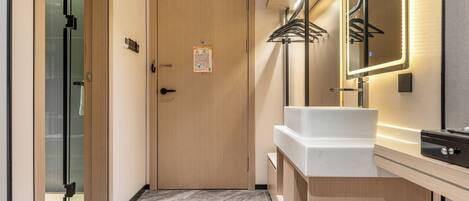 A modern bathroom with a wooden door, a white sink, a mirror with LED lights, and a glass shower enclosure.