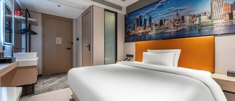 Et moderne hotelværelse med en stor seng, et bybillede på væggen, et skrivebord med en computer og et klædeskab.