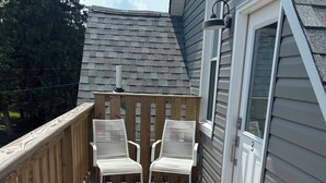 A wooden deck with two white chairs, a door with a number, and a welcome mat. - Main Stay on Market Unit 3 -Healthcare and Military Friendly (Mascoutah)