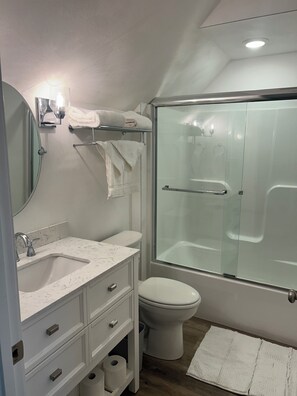 Une salle de bain moderne avec une douche à parois de verre, des toilettes blanches, un lavabo en marbre et un miroir.