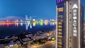 Un hôtel moderne, doté d’une enseigne bien visible, offrant une vue sur les gratte-ciel de la ville et donnant sur un plan d’eau où se reflètent les lumières.