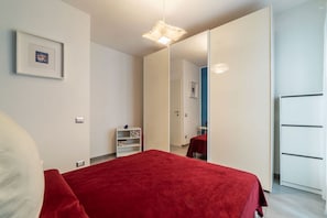 A bedroom with a bed, a wardrobe, a mirror, and a shelf with books.