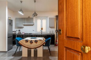 A modern kitchen with a dining table, chairs, pendant lights, and a wooden door.