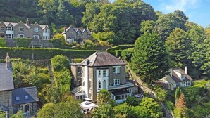A hillside residential area with stone houses, a prominent two-story house with a balcony, and a well-maintained garden. - The Cottage at Woodlands (Lynton)