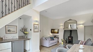 A modern kitchen with a built-in fridge, a dining area with a wooden table and chairs, and a living room with a sofa and a fireplace. - The Cottage at Woodlands (Lynton)