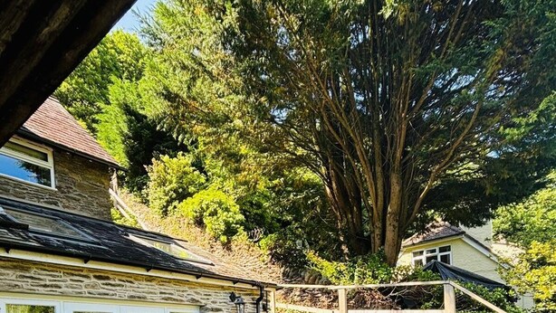 A stone house with a patio area featuring wicker furniture and a hot tub. - The Cottage at Woodlands (Lynton)
