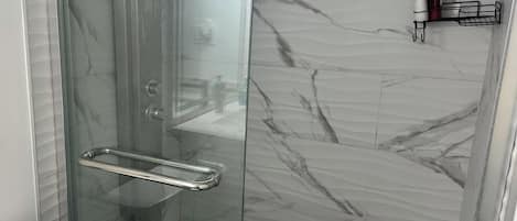Een douchecabine met glazen wanden, een roestvrijstalen handgreep, een wit toilet en een wand met een marmerlook.