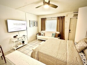 Een slaapkamer met een bed, een televisie, een bank en een plafondventilator.