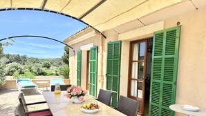 An outdoor patio with a table set for dining, wicker chairs, and a small round table. - Es Carritxó, Peace and Nature in Mallorca (Carritxo (Es))