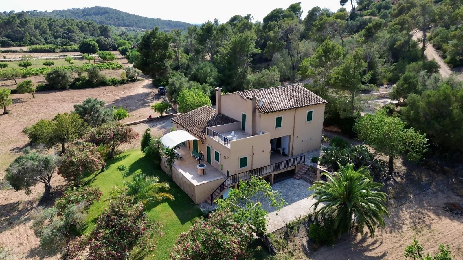 Une maison à deux étages avec un patio, entourée de verdure et d’arbres.