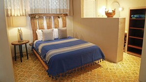 Un dormitorio con cama, mesita de noche, lámpara, ventana con cortinas, espejo y estante con adornos.